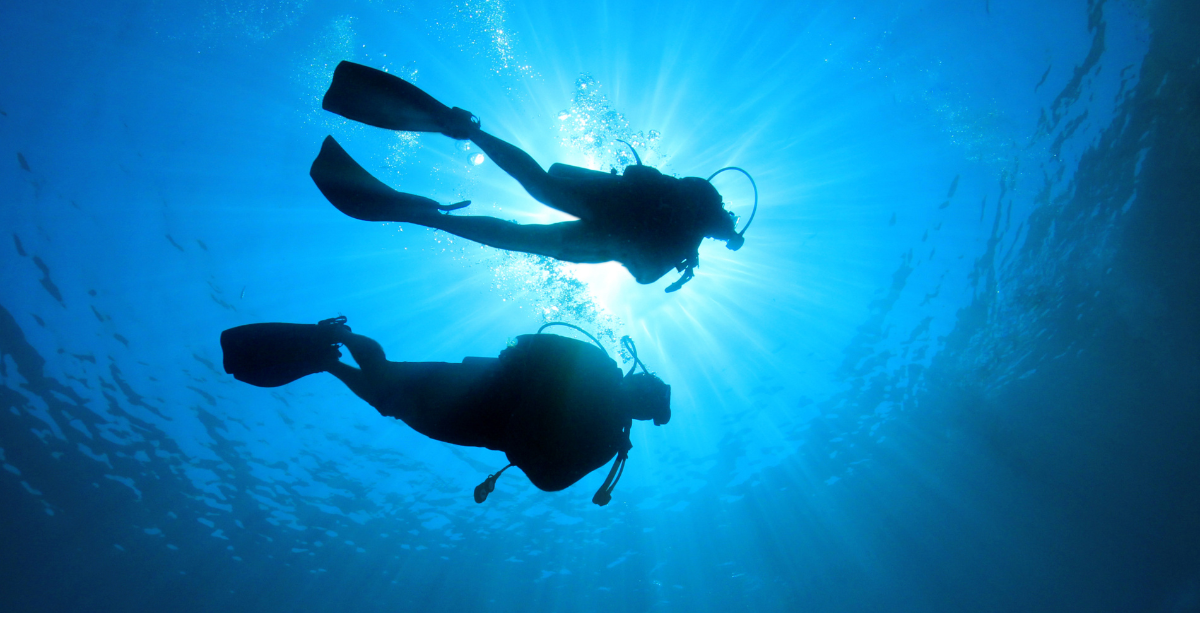 Silhouette of two divers near the surface of deep water